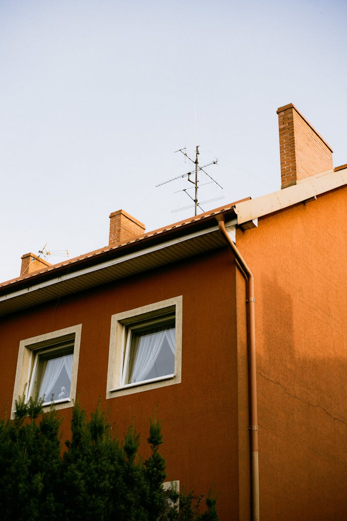 A brown suburban house with an antenna on the roof against a clear sky.